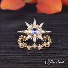 a gold ring with a blue stone in the center and white diamonds around it on a wooden surface