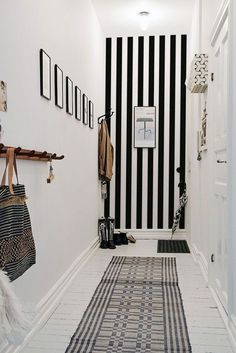 a hallway with black and white stripes on the wall, rugs and coat racks