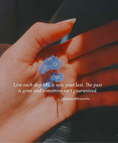 a woman's hand holding a small blue flower with the words live each day like it was your last the past is gone and tomorrow isn't quainted