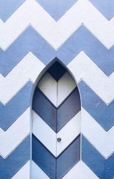 an open door in the middle of a blue and white chevroned wall with a clock on it