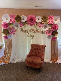 a chair sitting in front of a happy birthday sign and flowers on the wall behind it