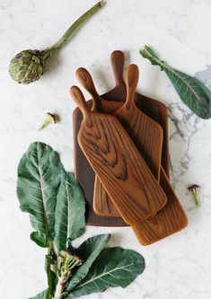 three wooden cutting boards sitting on top of a marble counter next to green leaves and flowers