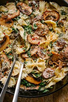 a skillet filled with pasta, mushrooms and spinach on top of a wooden table