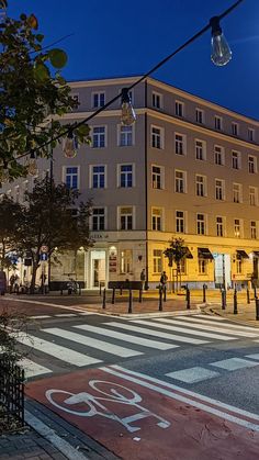 an empty street at night in front of a large building with lights on it's sides