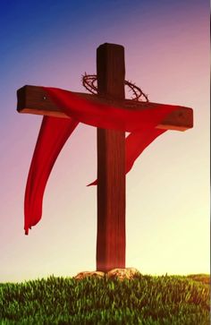 a wooden cross on top of a lush green field next to a red cloth draped over it