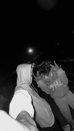 black and white photograph of two people standing on the street at night with one person covering his face