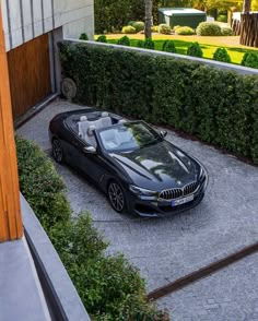 a black convertible car parked in front of a house next to a driveway and trees