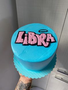 a person holding up a blue cake with the word libra on it in pink icing