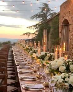 a long table is set with white flowers and candles for an outdoor dinner party in the evening