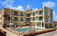 an apartment building with a swimming pool in the foreground and people lounging around