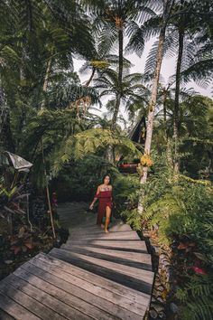 a woman walking across a wooden bridge surrounded by trees