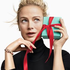 a woman holding a green box with a red ribbon around it and looking at the camera