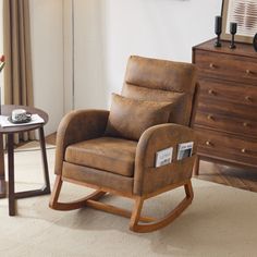 a living room with a rocking chair, table and dresser next to it in front of a window