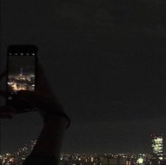 a person holding up a cell phone to take a photo of the city at night