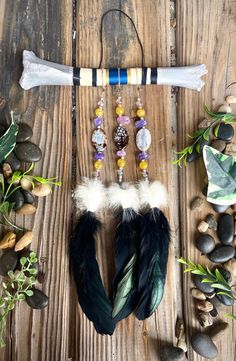 an assortment of beads and feathers on a wooden table next to rocks, plants and stones