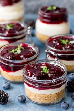 small jars filled with cheesecakes and berries on a blue tablecloth next to blackberries