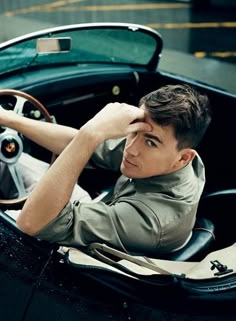 a young man sitting in the driver's seat of a vintage car, holding his hand to his head