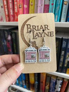 a pair of earrings with the words briar layne on them in front of bookshelves