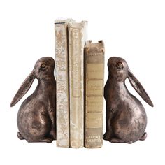 two metal rabbits sitting next to each other in front of books