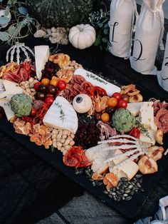 an assortment of cheeses, meats and vegetables on a black platter with pumpkins in the background