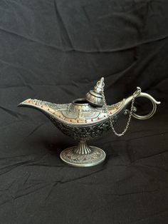 a silver teapot with a chain on it's neck and lid sitting on a black background