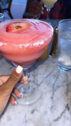 a person holding up a pink drink at a table