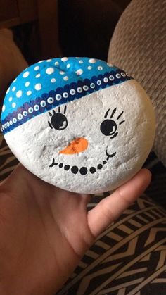 a hand holding a painted rock with a snowman face on it