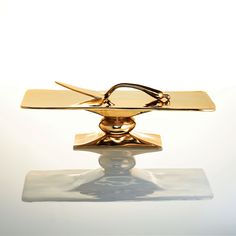 a pair of scissors sitting on top of a piece of gold metal object with a white background