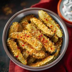 a bowl filled with fried pickles on top of a red cloth next to a cup of yogurt