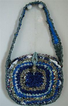 a crocheted bag hanging on a wall with a blue handle and looped handles