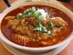 a bowl of soup with meat, noodles and garnishes on the side