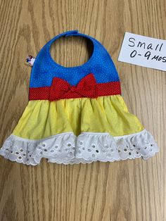 "Baby bib. Blue. Yellow. Red. Cotton. Batting, lace. Inspired by the Adorable Snow White! Your little beauty will look as adorable as Snow White!! Front and lining of bib is a soft two tone blue with tiny white dots. Skirt is yellow with tiny white dots. White lace ruffle at the bottom of skirt. Band and bow are red with tiny white dots. Princess ribbon. Snap closure. Perfect for baby drool and food messes. Protect baby's clothes. Bib has batting between cotton fabric layers for extra absorbency Cute Blue Bib For Playtime, Safe Laundry Detergent, Princess Snow White, Blue Yellow Red, Baby Protection, Fabric Glue, Lace Ruffle, Fabric Softener, Laundry Detergent