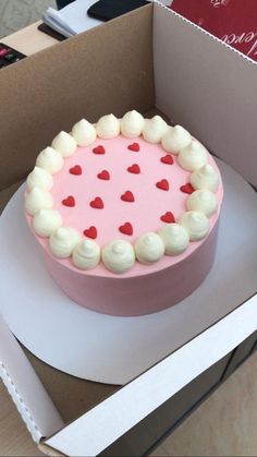 a pink cake with white frosting and red hearts on top in a cardboard box