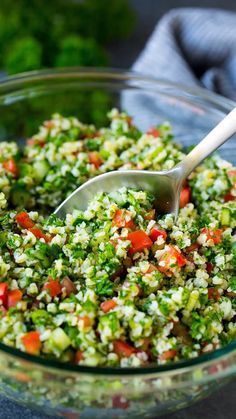 a bowl filled with rice and vegetables on top of a blue table cloth next to a silver spoon