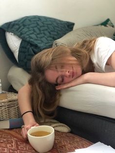 a woman laying on top of a bed next to a cup of coffee