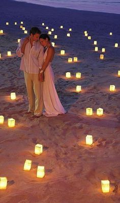 a man and woman standing in the sand surrounded by lit candles