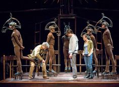 five people standing on stage with masks around their heads and hands, all looking at each other