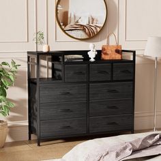 a black dresser sitting in front of a mirror on top of a wooden floor next to a lamp