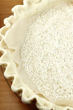 an uncooked pie crust with white rice in the middle on a wooden table