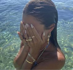 a woman covers her face with her hands in the clear blue water, while standing in shallow water