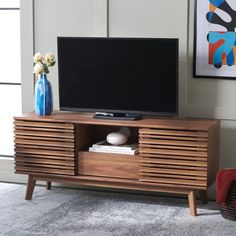 a flat screen tv sitting on top of a wooden entertainment center next to a vase with flowers