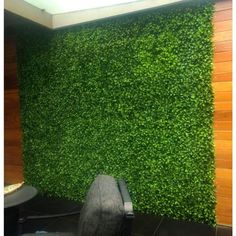 a chair sitting in front of a wall covered with green plants and grass growing on it's sides