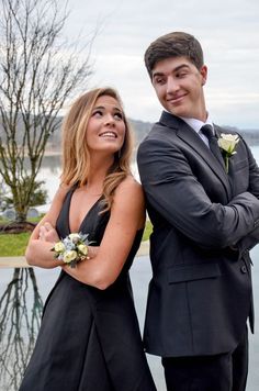 a man and woman standing next to each other in front of a body of water