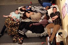 four people laying on top of a bed with their arms around each other while looking at an electronic device