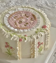 a cake decorated with pink and green flowers on a white table cloth covered in lace