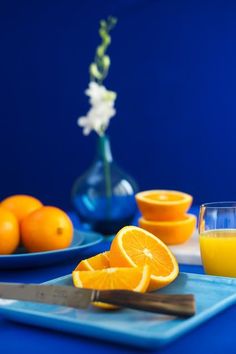 oranges and juice are sitting on a blue table with white flowers in a vase