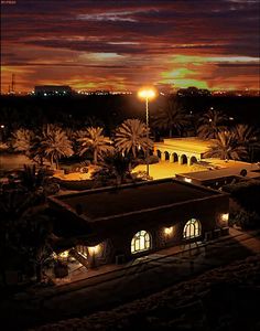 an aerial view of a building at night with lights on and palm trees in the foreground