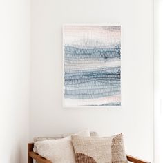 a wooden bench sitting next to a white wall with a painting on the wall above it