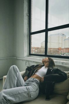 a woman laying on top of a white couch next to a window in a room