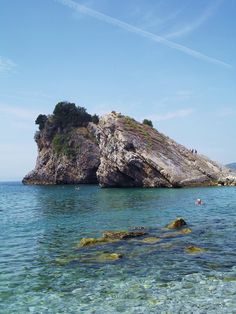 an island in the middle of the ocean with people swimming around and on top of it